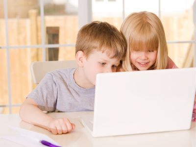 Two children looking at a laptop screen, smiling.