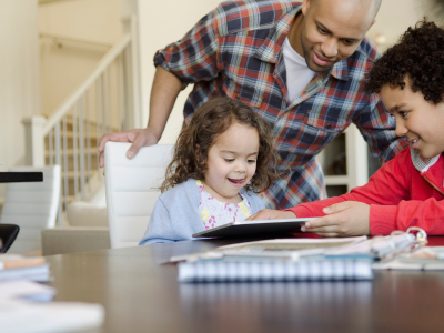 Little girl playing the iPad with her dad and brother.