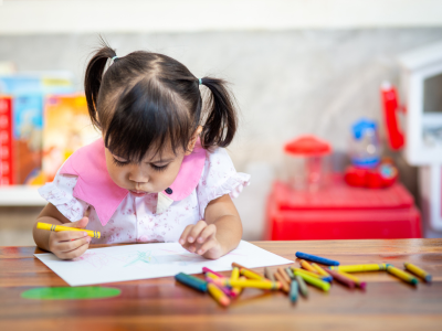 Child drawing on paper using crayons.