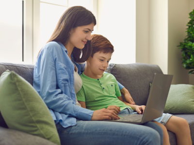 Parent and child, sat on the sofa and looking at a laptop.