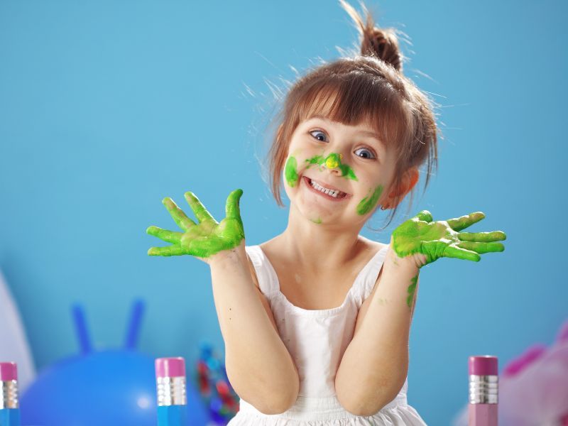 Happy-looking child with green paint on their hands and face.