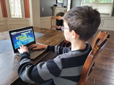 Child sitting at a table on laptop writing a story on Night Zookeeper.