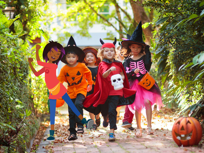 Children in Halloween costumes running down a path with Night Zookeeper Riya.